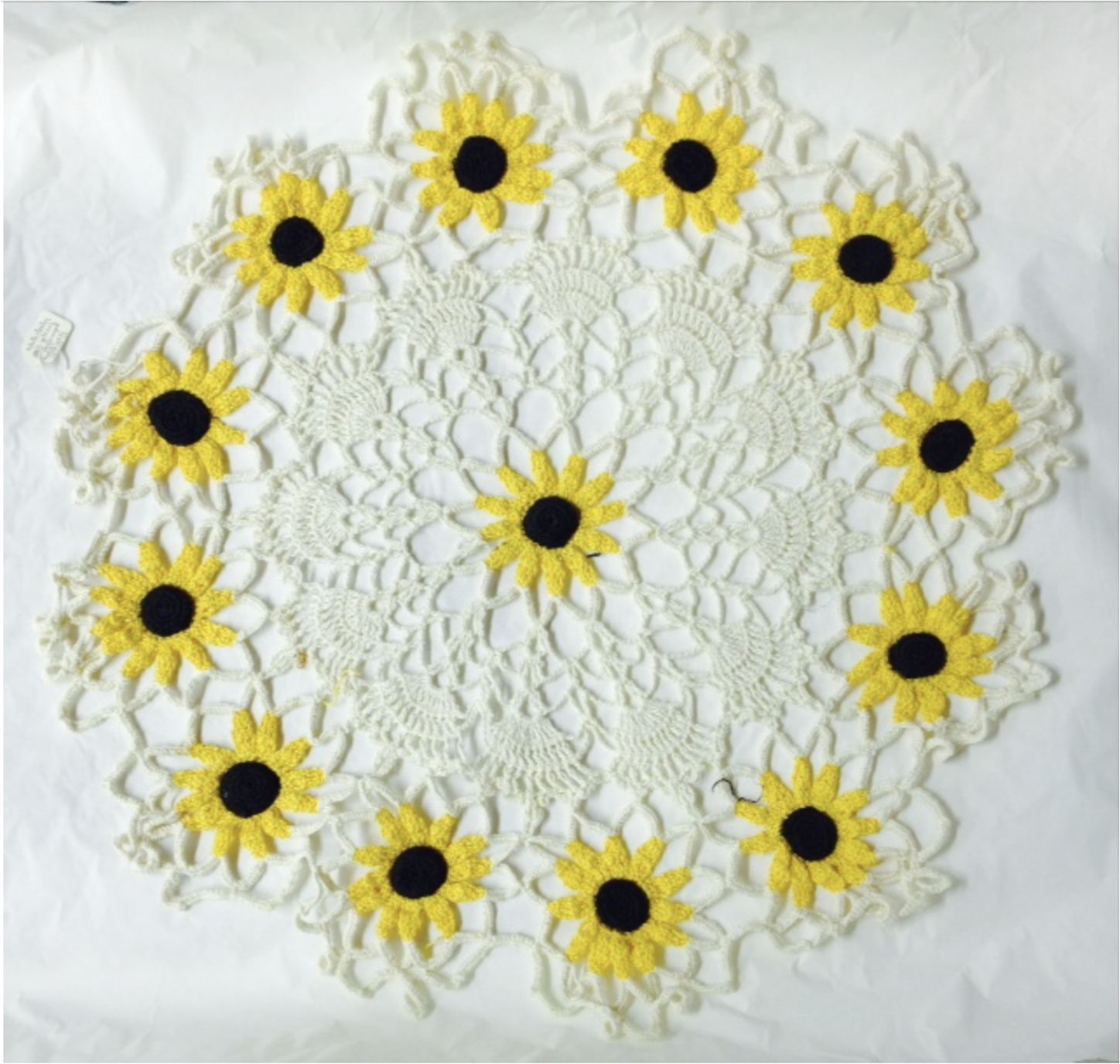 A crocheted doily on a white background with a pattern of yellow and black flowers