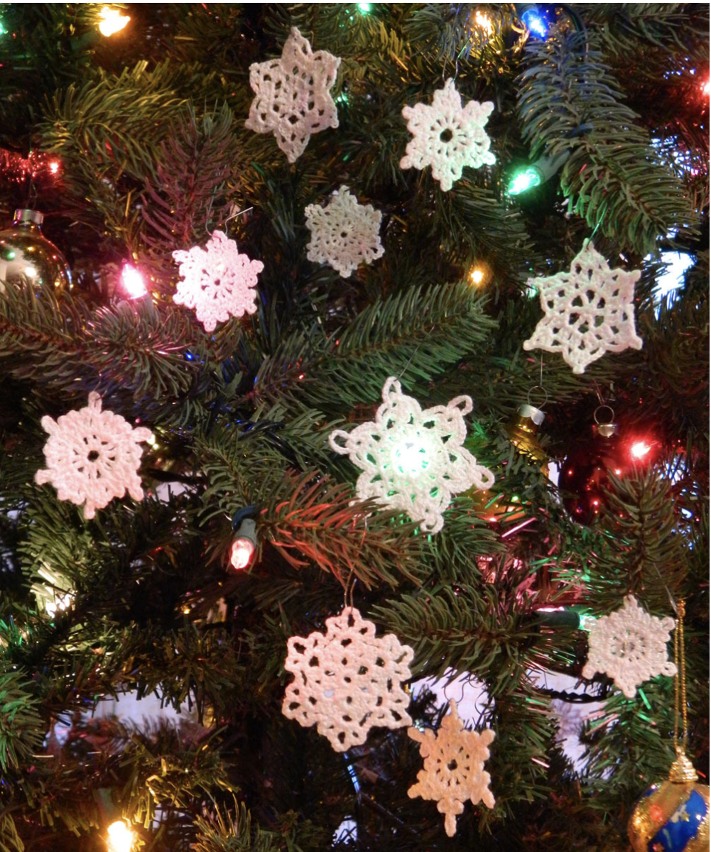 A close up image of crocheted snowflakes displayed on a pine tree with Christmas lights